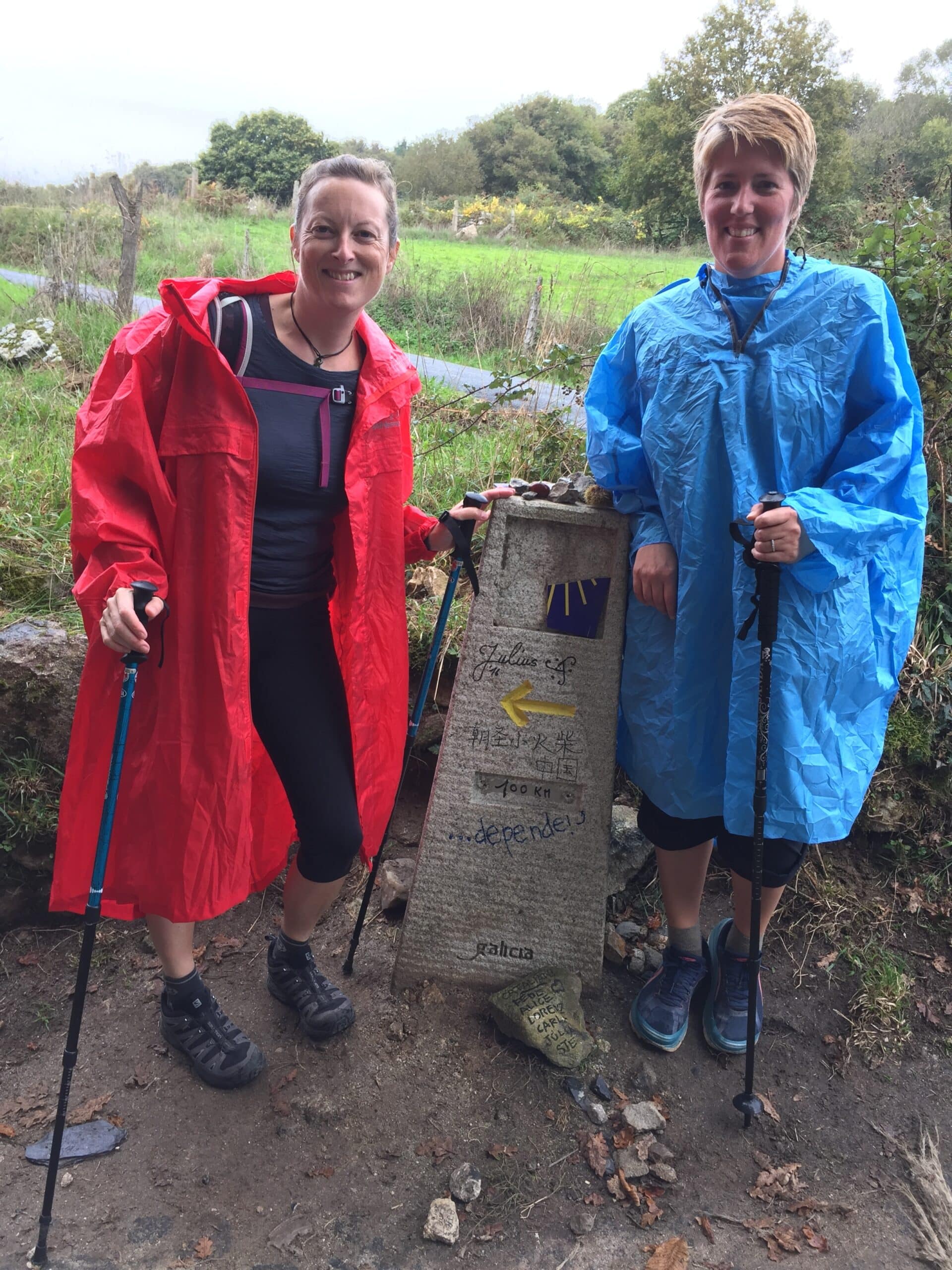 Two pilgrims in rain ponchos beside the 100 km marker in Galicia